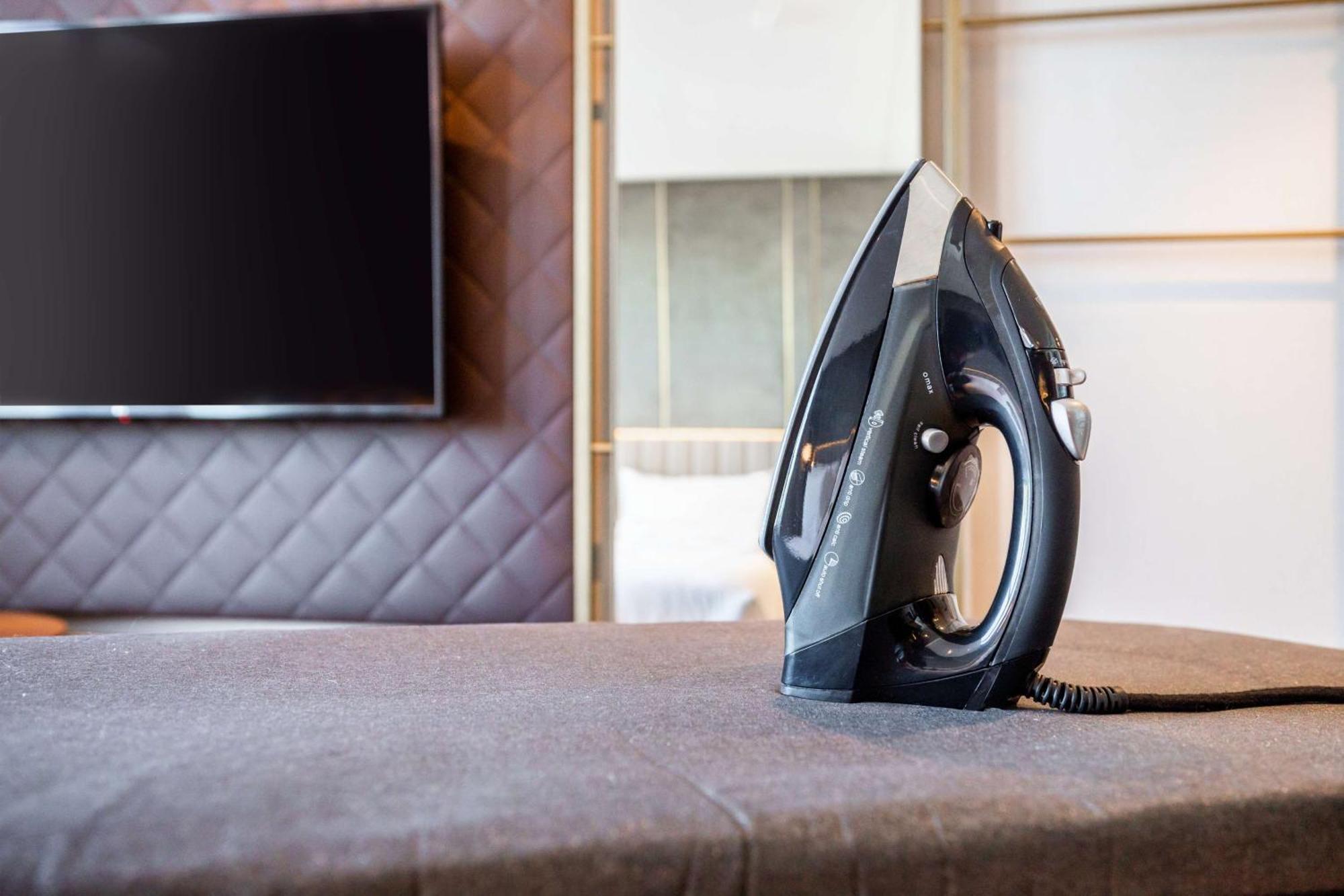 Nh Collection Copenhagen Hotel Ngoại thất bức ảnh The photo shows a black iron placed on a grey ironing board, which is covered with a fabric surface. In the background, there's a large television mounted on the wall, and the setting appears to be a modern room with stylish decor, featuring a quilte