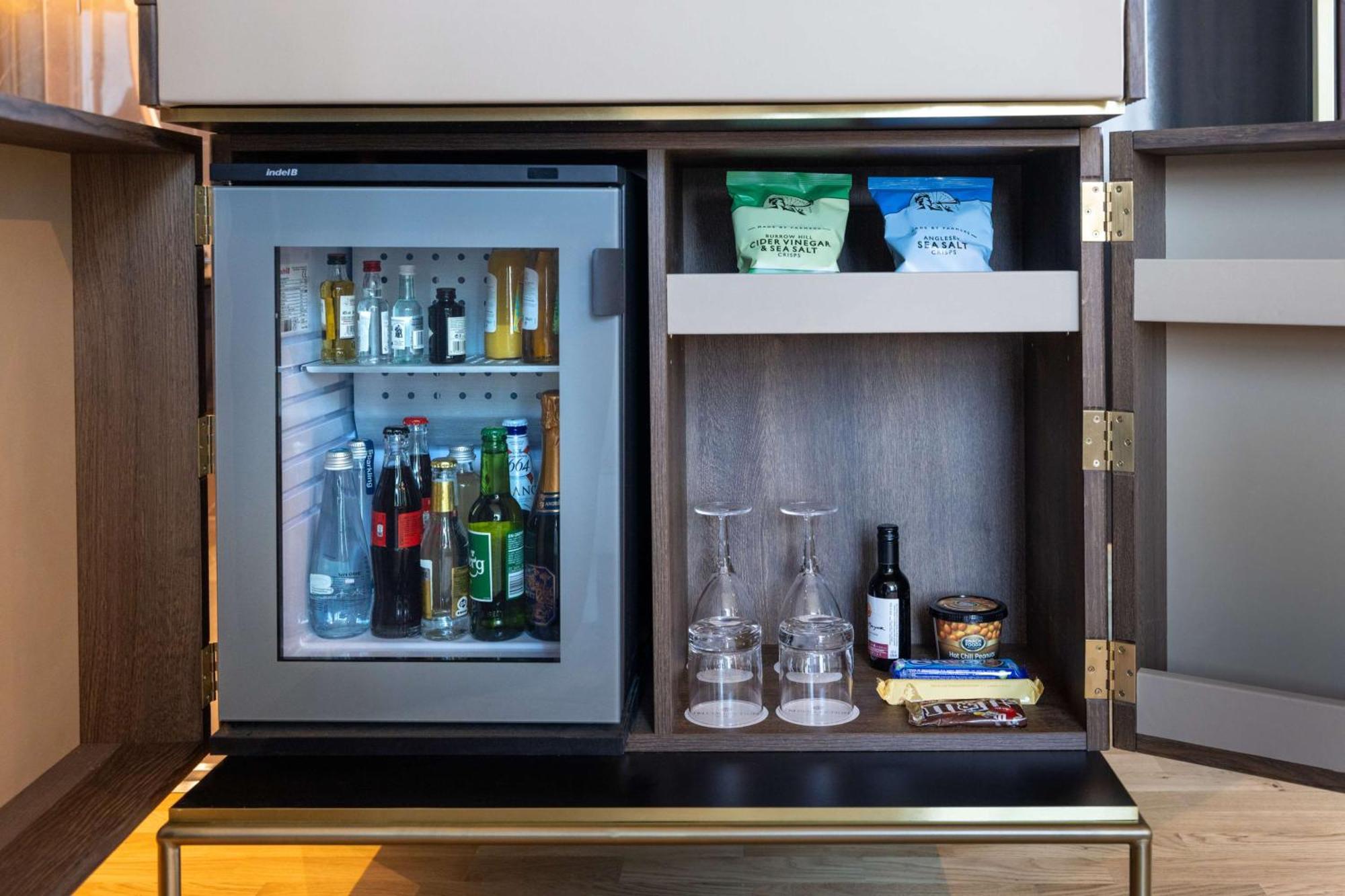 Nh Collection Copenhagen Hotel Ngoại thất bức ảnh The photo shows a stylish refrigerator integrated into a cabinet. The fridge has a glass door, allowing visibility of its contents, which include various bottles and drinks. Above the fridge, there are shelves with some snacks or food items organized